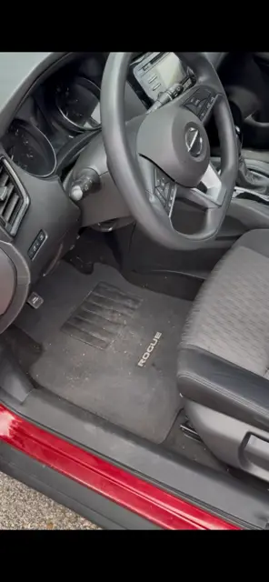 Driver footwell of a Nissan Rogue with a soiled floor mat and dust across the console
