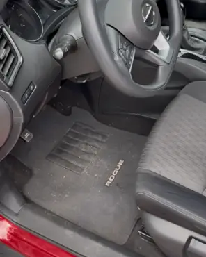 Driver footwell of a Nissan Rogue with a soiled floor mat and dust across the console